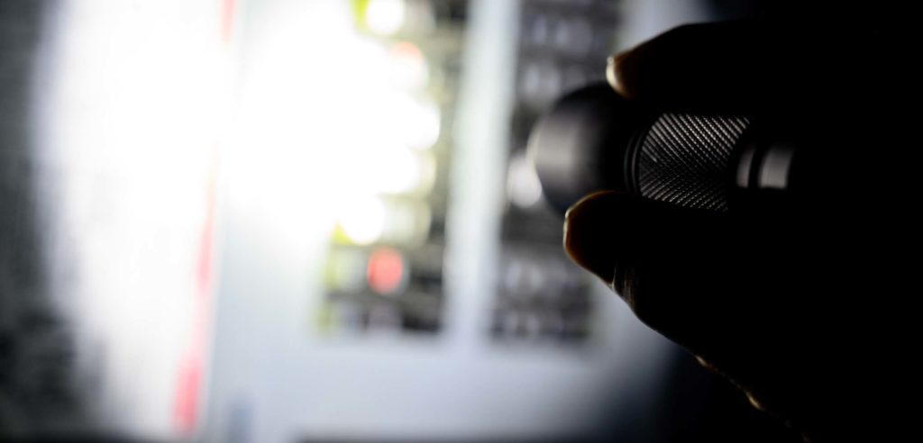 Flashlight inspecting electrical panel at night.