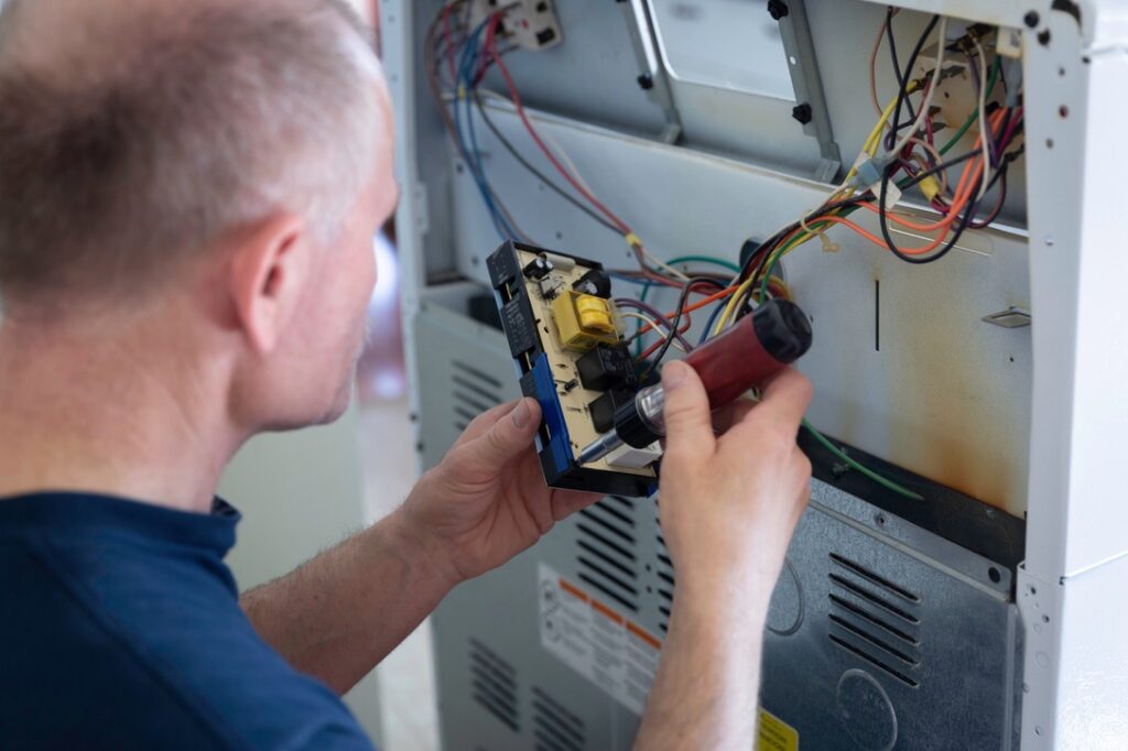 Hardwired vs Plug-In Appliances horizontal close up image of a caucasian adult male fixing the panel attaching wires at the back of an electric stove.