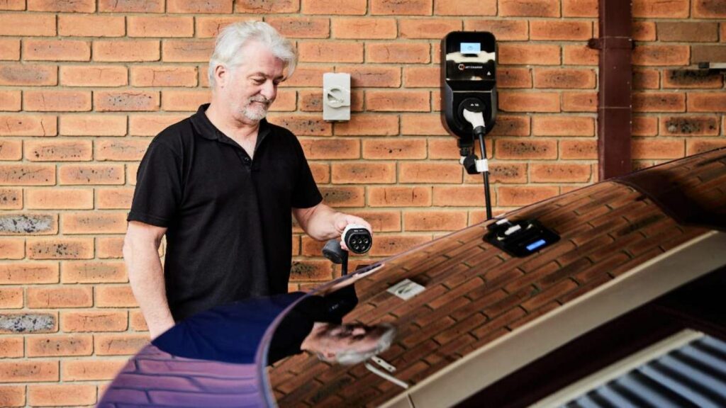 Older man using an electric vehicle charger at home