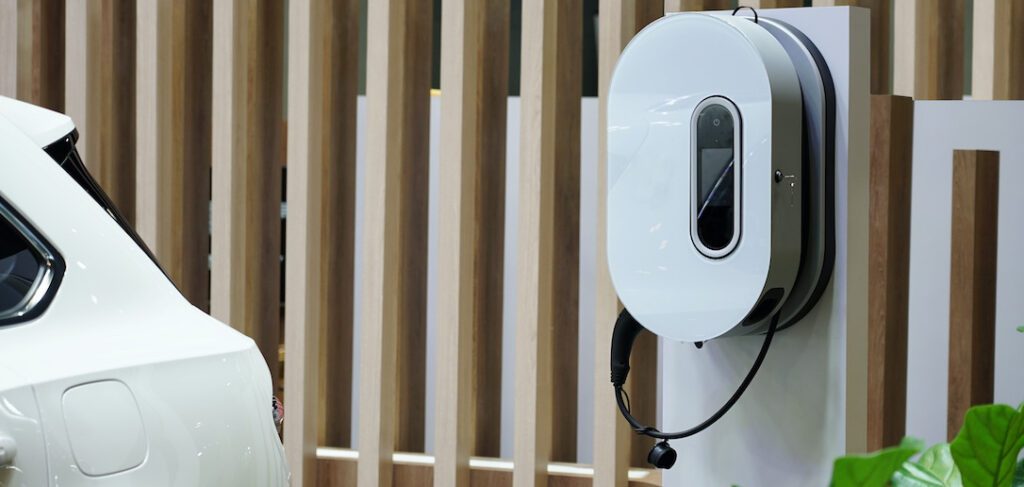 White electrical vehicle charger enclosure mounted outside near car